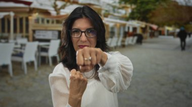 Beyaz bluzlu kadın, kalabalık caddede yumruk hareketinde kameraya sıkıca yumruk atıyor; güçlendirme.