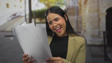 Eski şehirde belgelerle gülümseyen, mutluluk ve başarı sergileyen, gündüzleri dışarıda dururken gözlük takan ve iş kıyafeti giyen bir kadın..