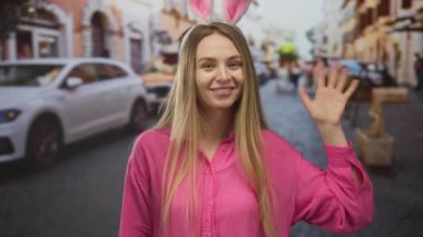 Pembe tavşan kulaklı genç bir kadın hareketli bir şehir caddesinde, canlı pembe bir gömlek giyip şehir hayatının ortasında neşeli bir paskalya teması yaratıyor..