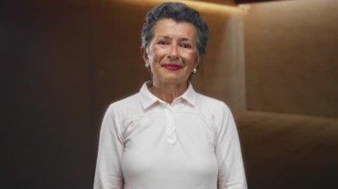 Beyaz gömlek giyen, duygularını ifade eden, rahat bir ortamda sıcak ve samimi bir an yakalayan, bir odada gri saçlı yaşlı bir kadın..