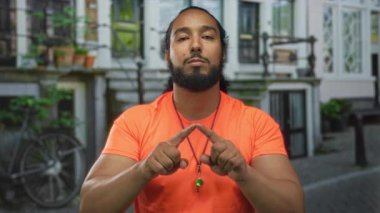 Adam sokakta ıslık çalan bir kolye takarken kamerayı işaret ediyor. Kendine güveni tam..