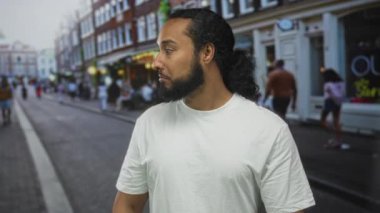 İşlek bir caddede beyaz tişört ve at kuyruğu giymiş sakallı bir adam kenar mahalleli meraklısı..