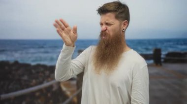 Beyaz gömlekli genç beyaz bir adam deniz kenarında kızıl sakallı bir yelpaze ile burun buruna yürüyordu..