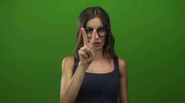 Gözlüklü İspanyol kadın yeşil ekran stüdyo profilinde kolunu kaldırıyor ve parmağını işaret ediyor..