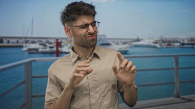 Adam, güneşli liman limanındaki liman iskelesinde beyaz teknenin tiksindirici ifadesiyle avuçlarını itiyor..