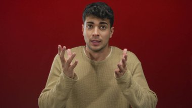 Erkekler, arka plan kırmızısı ve endişeli ifade ile genç İspanyol erkeğin stüdyo portresinde el kaldırır..