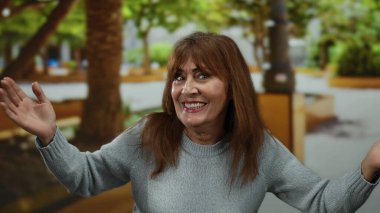 Kıdemli İspanyol kadın yeşil ağaçlarla parkta neşeyle dans ediyor. Mutluluk ve özgürlük sergiliyor..