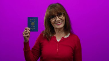 Gözlüklü yaşlı İspanyol kadın gülümsüyor, elinde pembe bir arka plana karşı Japon pasaportu var, seyahat ve kimlik teması öneriyor..