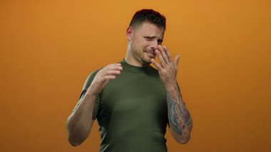 Dövmeli genç adam canlı turuncu arka plana karşı rahatsızlığını ifade ediyor. Duygularını ve tarzını aktarıyor..