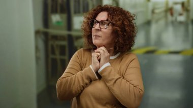 Orta yaşlı, kıvırcık saçlı ve gözlüklü bir İspanyol kadın gün boyunca şehir sokaklarında endişeli görünüyor..