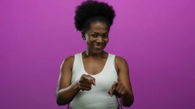 İzole edilmiş pembe arka planda parmak hareketleriyle gülümseyen kadın, modern stüdyo ortamında anlamlı duygular ve canlı kişiliğin altını çiziyor..