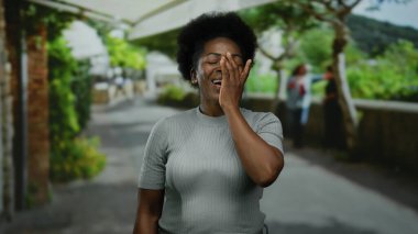 Arka planda yeşillik olan bir şehir caddesinde el ele gülen bir kadın samimi bir neşe anı yakalıyor..