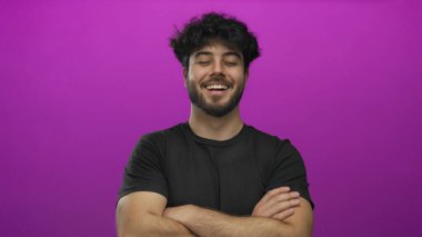 Sakallı İspanyol genç adam gülümsüyor ve kollarını pembe bir arka plana yaslıyor. Kendine güveni ve karizması var. Profesyonel ya da günlük kullanım için ideal..