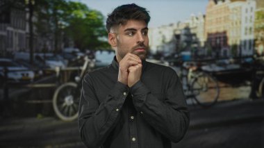 Genç İspanyol adam, Kanal Caddesi 'nin kenarında çenesinin altında gergin bir ifadeyle ve gergin bir duruşla el ele tutuşmuş duruyor; korku..