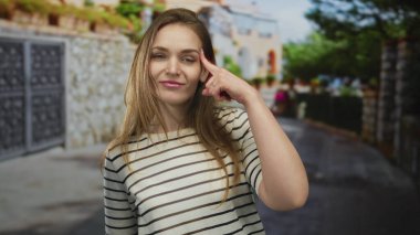 Yoğun bir şehir caddesinde, çizgili tişörtlü ve hafifçe sırıtan genç bir kadın, tefekkür.