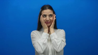 Beyaz gömlekli İspanyol kadın, canlı mavi bir duvara karşı şaşkınlığını ifade ediyor. Yüz ifadeleri ve el hareketleriyle değişik duygusal tepkiler gösteriyor..