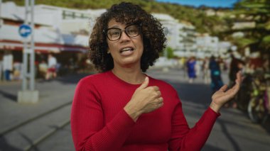 Gözlük takan kadın, güneşli caddede avuçlarını ileri doğru açıyor; sunum güven nişan bağlantısı.