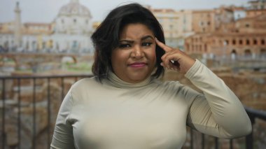Roma harabelerinin önünde esprili bir şekilde el kol hareketi yapan kadın, büyük boy Latin bir kadının tarihi bir şehirde neşeli bir ifade sergilediği açık hava sahnesini çekiyor..