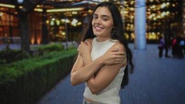 Gece yarısı apartman ışıkları altında çıplak kollarıyla sokakta çıplak kollarını saran bir kadın, kendinden memnun..