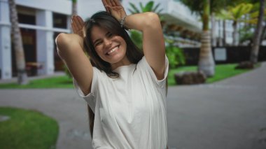 Genç İspanyol kadın neşeli tavşan kulakları yapıyor canlı bir şehir caddesinde jest yapıyor, neşe saçıyor ve tasasız anların özünü yakalıyor..