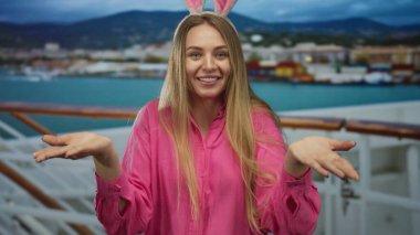 Bir yolcu gemisinde tavşan kulaklı bir kadın açık hava ortamında bir liman zeminine gülümsüyor pembe bir gömlek giyiyor, manzaralı bir yolculukta neşeli bir paskalya temasını somutlaştırıyor.