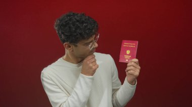 Avusturalya pasaportu tutan ve stüdyoda vize bilgilerini okuyarak çeneye dokunan İspanyol genç adam..