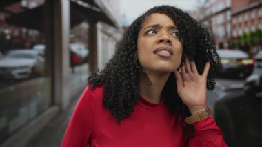 Yoğun bir şehir caddesinde trafiğin geçtiğini duymaya çalışırken kadın başını eğip başını eğiyor; merak.