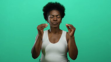 İzole edilmiş yeşil bir arkaplanda jestler yapan kadın, hareket yoluyla ifade ve duygu gösterir, bireyselliği ve kültürü vurgulayan canlı bir fotoğrafta yakalanır..