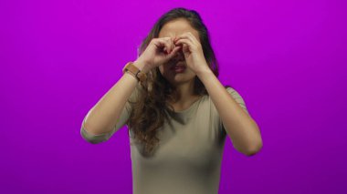 Genç İspanyol kadın pembe stüdyoda gözlerini nazikçe ovalıyor. Günlük bol bej gömlek giyiyor. Yorgunluk giderici..