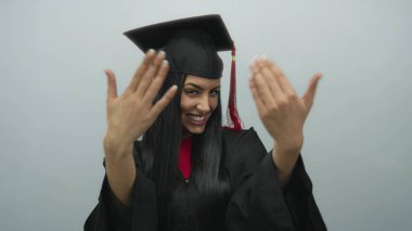 Mezuniyet elbisesi giymiş İspanyol kadın izole edilmiş beyaz bir arkaplan önünde gülümsüyor ve dışarı uzanıyor, akademik başarının neşeli anını yakalıyor..