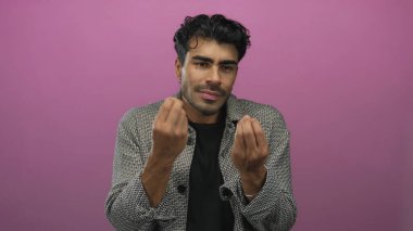 Adam pembe bir stüdyoda siyah gömlek ve kareli ceket giyerken gergin hareketler sergiliyor..