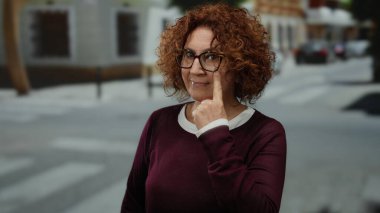 Gözlüklü esmer kadın, şehir merkezinde düşünceli ve konuşkan bir davranış sergiliyor..