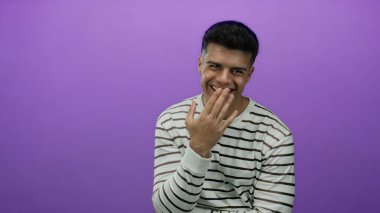 Genç adam el üstünde gülüyor, çizgili süveter giyiyor, canlı mor bir arka plana karşı, bir stüdyo ortamında neşeli bir ifade sergiliyor.