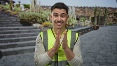 Yansıtıcı yelek giyen İspanyol genç adam parktaki merdivenlerde gönüllü olarak duruyor..