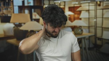 Sakallı genç bir adam bir lamba dükkanında boyun rahatsızlığı yaşıyor. Etrafı çeşitli aydınlatma armatürleriyle çevrili ve evde hayal kırıklığı ve acı dolu bir ortam sergiliyor..