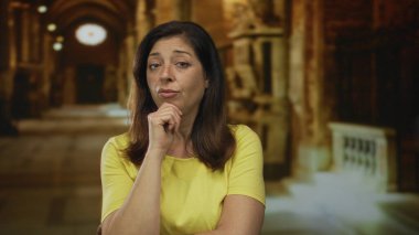 Sarı gömlekli kadın, yumuşak ışıklarla aydınlatılmış kilise binasında el üstünde dinleniyor; tefekkür.