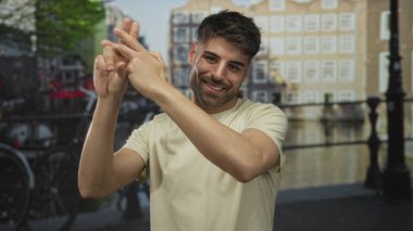 Genç İspanyol adam, kanal binalarının yanındaki kaldırım taşı sokakta birbirine dolanmış parmakları olan bir hashtag işareti yapıyor..