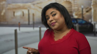 Kadın, arka planda tarihi bir mimariyle şehir merkezini işaret ederken gülümsüyor, açık şehir ortamına duyduğu güveni dile getiriyor.