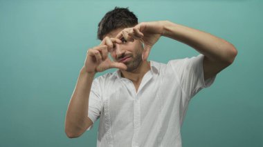 Beyaz tişörtlü genç İspanyol adam turkuaz bir stüdyoda elleri ile çekim; yaratıcılığa odaklanma.