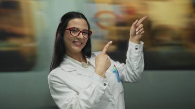 Kırmızı gözlüklü kadın kapalı mekanda durup bulanık tren istasyonunu işaret ediyor..