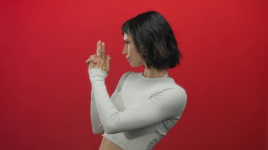 Latin kökenli genç bir kadın kırmızı stüdyoda kameraya silah doğrultuyor..