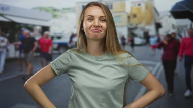 Hareketli bir şehir caddesinde rahat bir şekilde dikilen kadın, günlük giysiler içinde, hayat dolu şehir zemininin ortasında kendine güvenin ve sevincin ifadesini canlandırıyor..