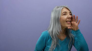 Gri saçlı yaşlı kadın, izole bir mor arka plan duvarına karşı konuşuyor. Duygularını ve ifadelerini aktarıyor..