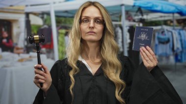 Elinde tokmak ve Avustralya pasaportu olan üniformalı bir kadın yargıç dükkan geçmişi olan açık pazar caddesinde duruyor..