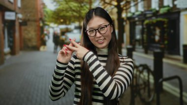 Açık havada gülümseyen bir kadın canlı bir şehir caddesinde hashtag jesti yapıyor. Gençlik enerjisini ve modern iletişimi somutlaştırıyor..