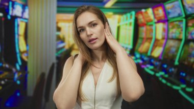 Genç bir kadın, kalabalık kumarhanedeki neon ışıklarının altında slot makinesinde iki eliyle kulaklarını kapatıyor; gürültü stresi.