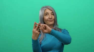 İzole edilmiş yeşil arka plan duvarına işaret eden gri saçlı yaşlı kadın modern iletişim ve sosyal etkileşimi somutlaştırıyor..