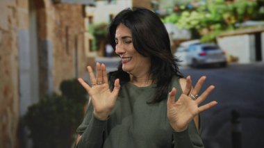 Olive Top giyen orta yaşlı İspanyol kadın, eski bir kasabanın kaldırım taşı sokağında elleri ile reddedilme jesti yapıyor..