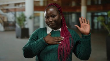 Afro-amerikan kadın yemin jesti yapıyor açık hava süveter ayarlı pembe örgülü, samimiyetini ve odaklanmasını iletiyor.