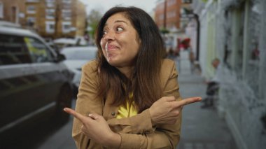 İşlek bir şehir caddesinde sarı gömlek ve kahverengi ceket giyerken her iki işaret parmağı olan bir kadın, kararsızlık şüphesi.